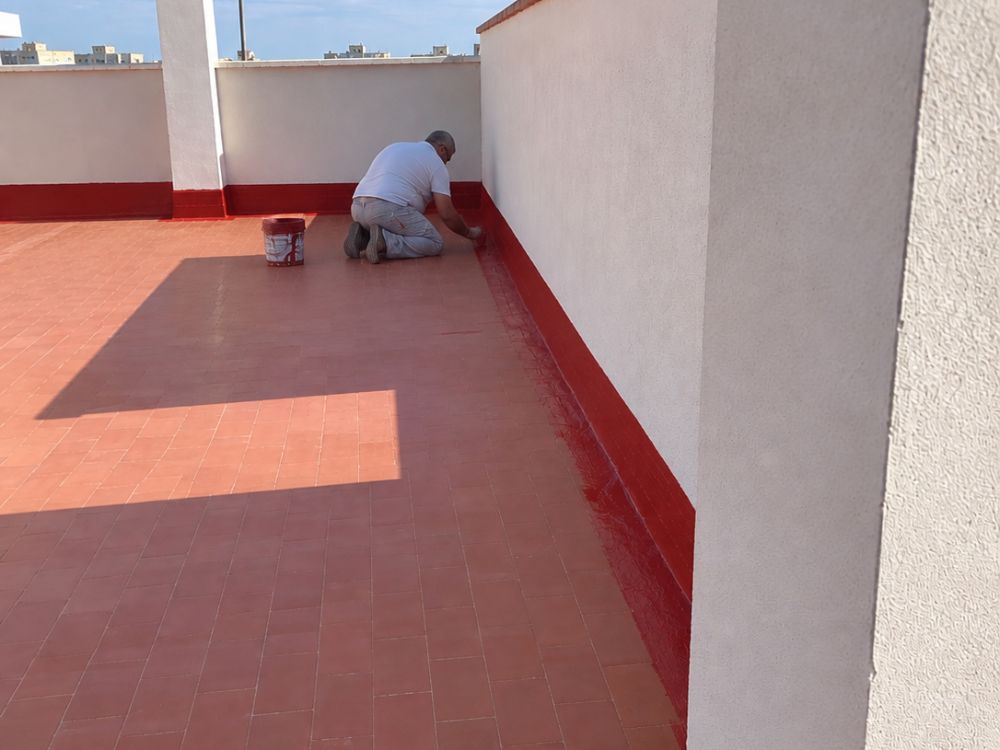Operario de Pinturas Pizarro aplicando el sistema impermeabilizante en el encuentro del peto con el pavimento
